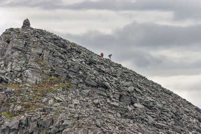 Distant view of hikers climbing mountain against cloudy sky