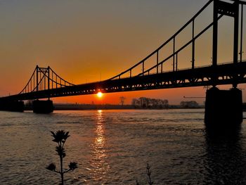 Silhouette bridge over river against sky during sunset