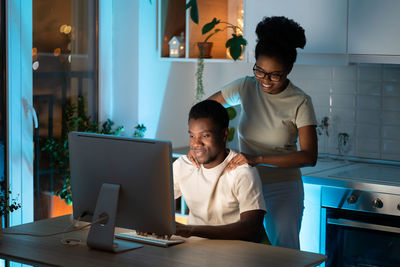 Loving african woman massaging shoulders of husband while he working late on computer at home