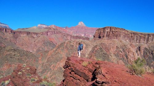 Man standing on rocky mountain against clear blue sky