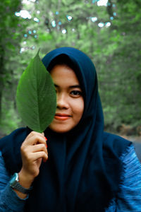 Portrait of smiling woman wearing hijab holding leaf