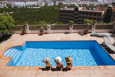 Female friends wearing sun hats sitting at poolside on sunny day