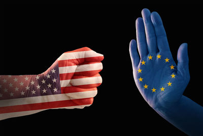 Cropped hands with american and european union flags painted against black background