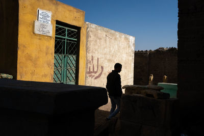 Rear view of man standing by building against clear sky