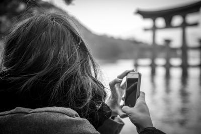 Rear view of woman using mobile phone at lake