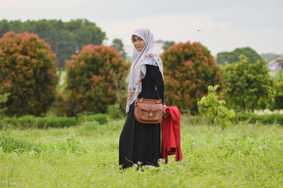 Portrait of smiling woman in hijab standing on field 