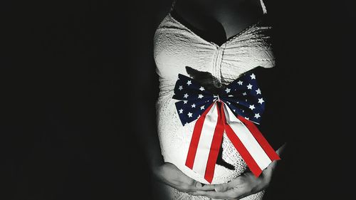 Pregnant woman with american flag tied bow on cloth against black background