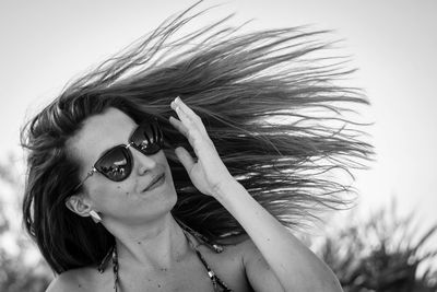 Young woman wearing sunglasses while tossing hair against sky