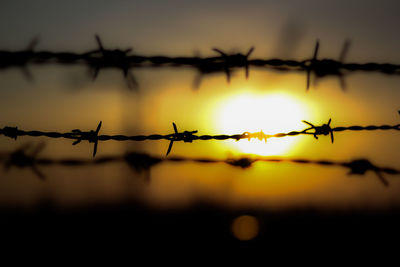 Close-up of silhouette barbed wire against sky during sunset