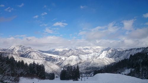 Scenic view of snowcapped mountains against cloudy blue sky on sunny day