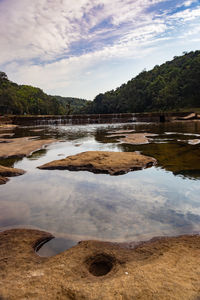 Riverbed stone hole with water and surrounded by green forests from flat angle