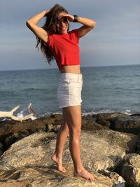 Rear view of woman standing at beach against sky during sunset