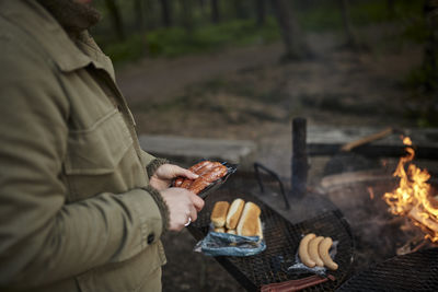 Person holding sausages, campfire in background