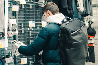 A young guy with a backpack chooses an accessory in a store.