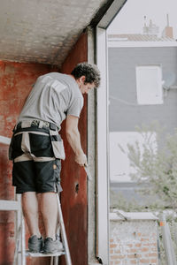 A young caucasian man repairs a window opening while standing on a metal stepladder