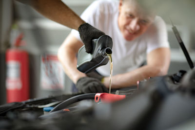 Cropped hand of mechanic pouring oil in car