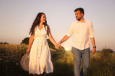 Couple holding hands while standing on land against sky during sunset