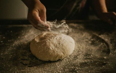 Cropped hand of person making dough at kitchen