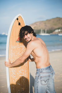 Midsection of shirtless boy at beach against sky