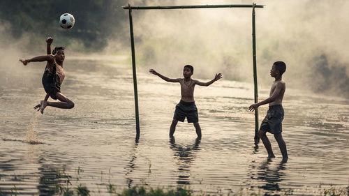 Shirtless boys playing soccer in lake