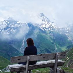 Rear view of woman sitting on bench against mountain range