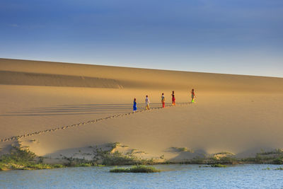 Distant view of women walking at desert by lake against blue sky