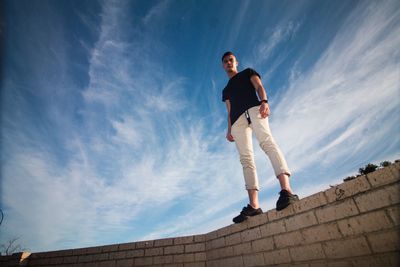 Low angle view of man standing on retaining wall against sky