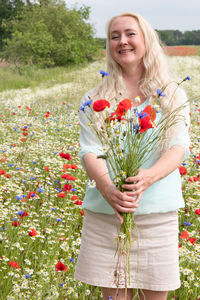 Beautiful middle-aged blonde woman stands among a flowering field of poppies