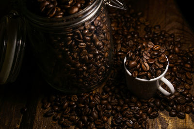 Roasted coffee beans in glass jar and cup on table