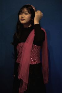 Portrait of young woman standing against blue background