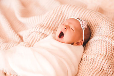 Newborn girl with headband yawning on bed