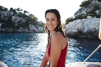 Portrait of happy woman in swimwear sitting on boat against clear sky during sunset