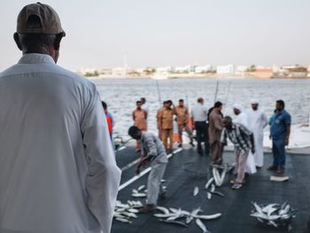 Rear view of people standing by sea against sky