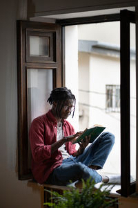 Upset black man excited from reading sits on windowsill with dramatic book worries about characters.
