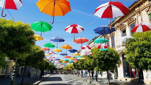 Multi colored umbrellas hanging on street in city against sky