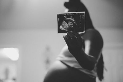 Side view of pregnant woman showing ultrasound photograph at home