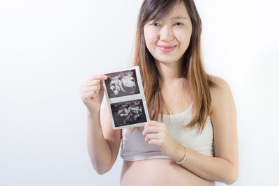 Portrait of smiling pregnant woman holding medical x-ray on stomach