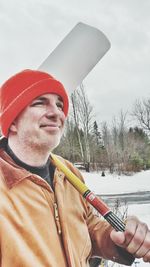 Smiling man holding shovel against sky during winter