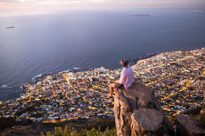 Rear view of man sitting on rock by sea