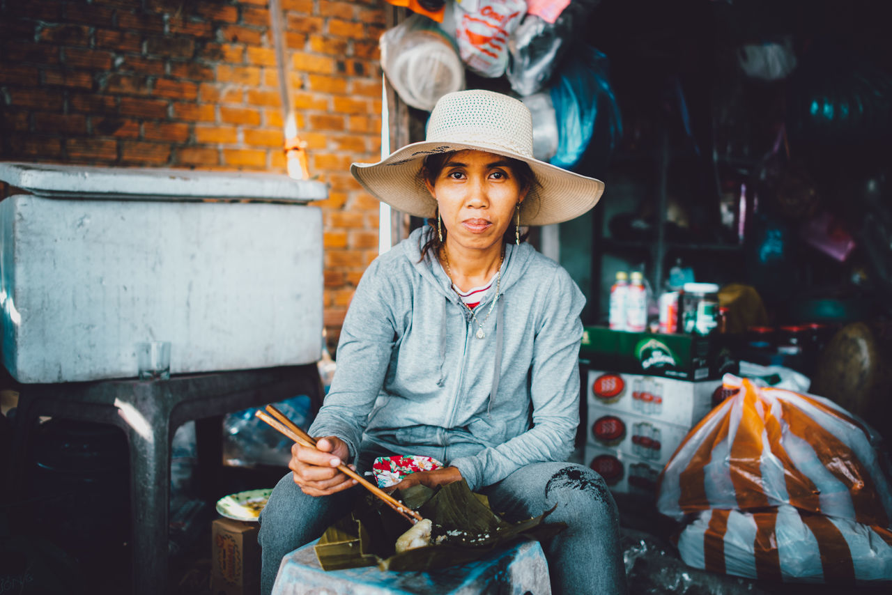 hat, one person, sitting, clothing, front view, real people, lifestyles, casual clothing, leisure activity, holding, three quarter length, focus on foreground, day, technology, adult, mobile phone, connection, portrait, cowboy hat