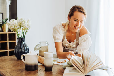 Woman reading book of recipes while cooking at kitchen table