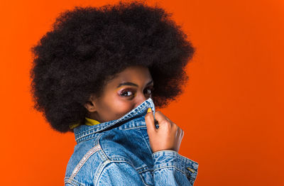 Close-up portrait of young woman against orange background