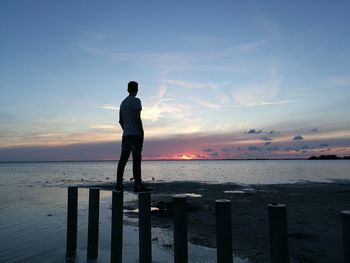 Low angle view of man standing on wooden post at beach against sky