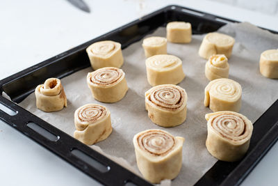 Freshly made cinnamon rolls on the baking tray, christmas tree with lights on the background, fe