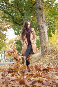 Low angle view of woman wearing coat walking on autumn leaves in park