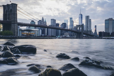 Bridge over river by buildings against sky in city