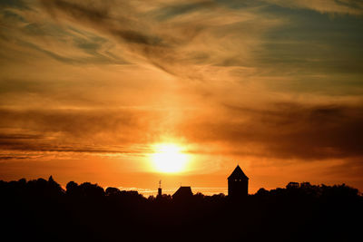 Silhouette buildings against dramatic sky during sunset