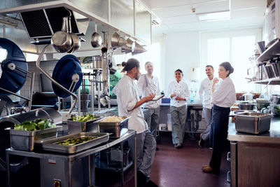 Male chef holding digital tablet while discussing with colleagues in commercial kitchen