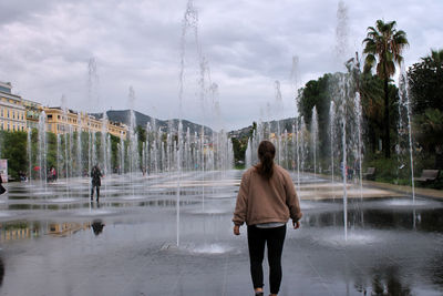 Rear view of woman walking on fountain in rainy season