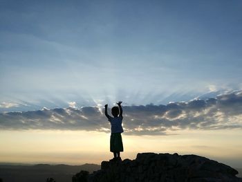 Carefree boy standing on rock against sky during sunset